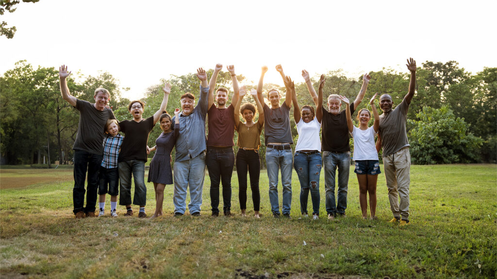 A diverse non-profit group of people in a park cheering with their hands up